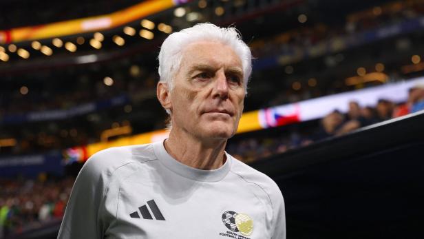 Hugo Broos, Trainer der südafrikanischen Fußballnationalmannschaft, trägt ein graues T-Shirt mit dem Logo der South African Football Association.