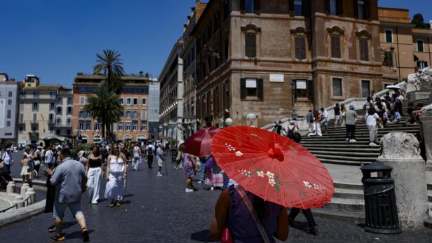 Eine Person mit einem roten Sonnenschirm geht über die Piazza di Spagna in Rom vor der Spanischen Treppe.