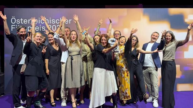 Gruppe von Menschen feiert auf einer Bühne vor der Aufschrift „Österreichischer Filmpreis 2026“.