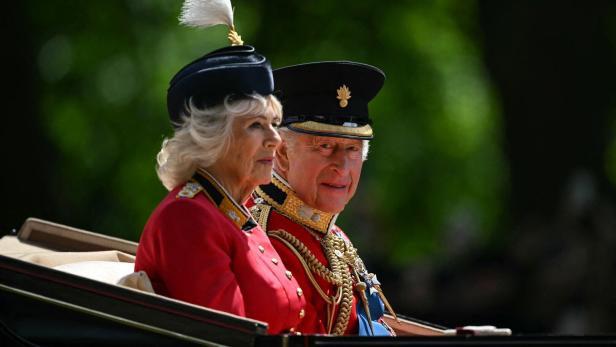 König Charles III. und Königin Camilla sitzen in einer Kutsche und tragen ihre traditionellen roten Uniformen.