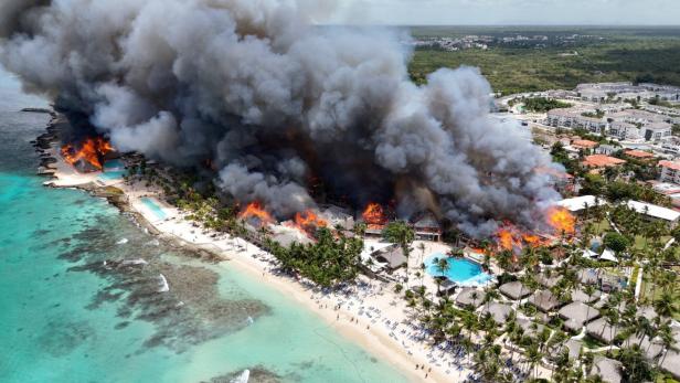 Großbrand in einer Strandhotelanlage mit dichtem Rauch über brennenden Gebäuden am Meer.