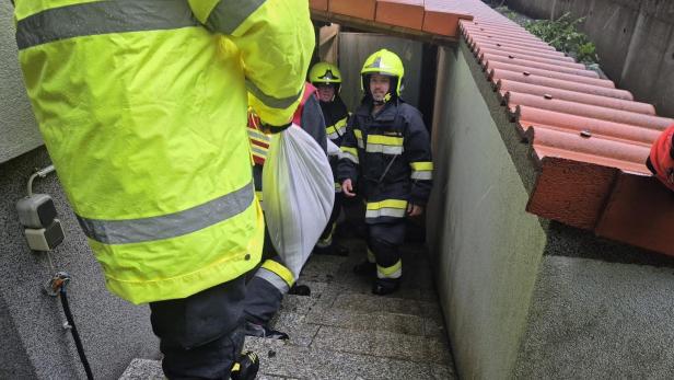 Feuerwehrleute tragen Sandsäcke durch einen engen Kellerabgang.