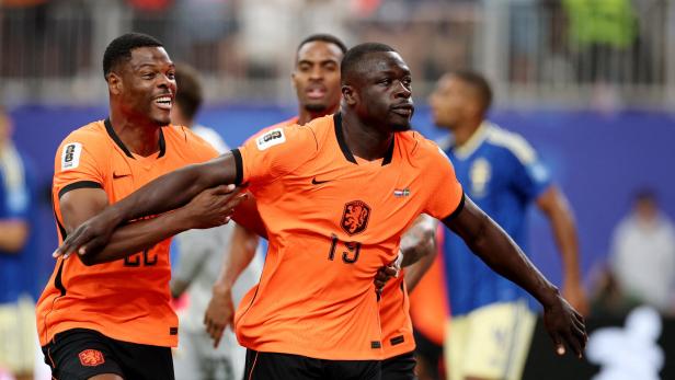 Zwei niederländische Fußballspieler in orangefarbenen Trikots feiern gemeinsam auf dem Spielfeld.