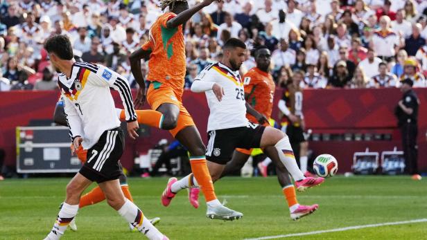 Fußballspiel mit Deutschland gegen die Elfenbeinküste, mehrere Spieler kämpfen um den Ball vor voller Tribüne.