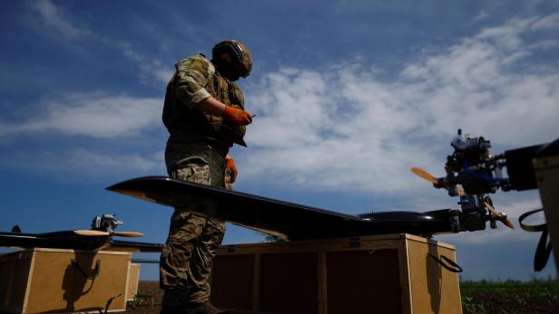 Soldat in Tarnuniform prüft ein Fluggerät auf Kisten unter blauem Himmel.