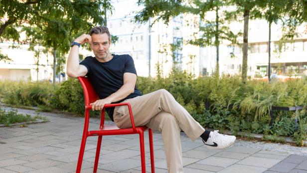 Jakob Seeböck sitzt entspannt auf einem roten Stuhl im Park.