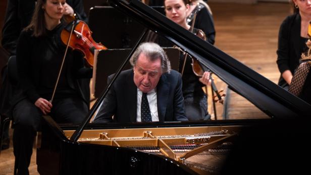 Ein Pianist spielt konzentriert auf einem Steinway-Flügel, begleitet von einem Orchester mit Streichern.