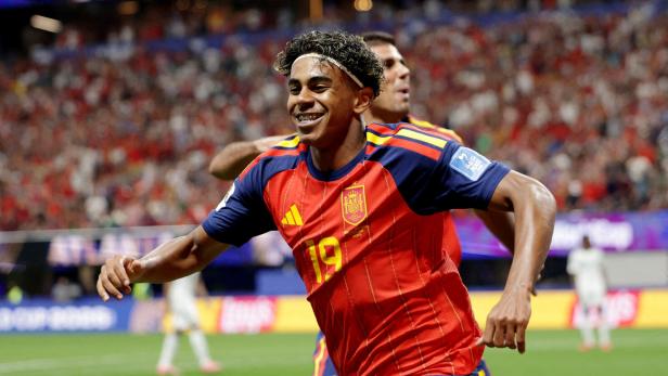 Lamine Yamal jubelt in einem roten Trikot der spanischen Nationalmannschaft auf dem Fußballfeld.