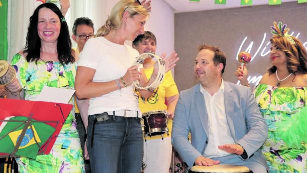 Gruppe feiernder Menschen mit brasilianischen Fahnen, mehrere halten Instrumente, ein Mann spielt Trommel.