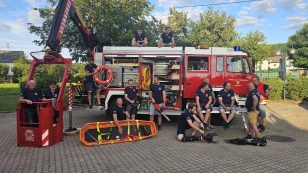 Mehrere Feuerwehrleute stehen und sitzen an einem roten Einsatzfahrzeug mit Rettungsgerät und geöffneter Geräteraumklappe.