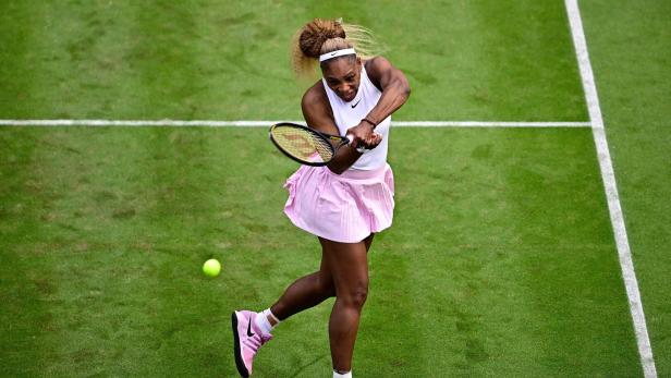Serena Williams schlägt auf einem Rasenplatz einen Tennisball mit ihrem Schläger zurück.