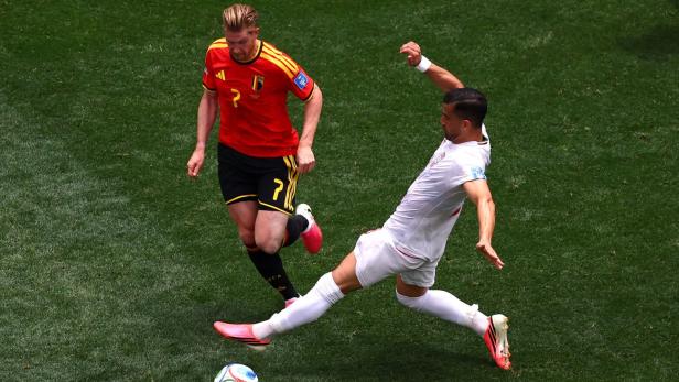 Kevin De Bruyne im belgischen Trikot kämpft auf dem Rasen um den Ball gegen einen Gegenspieler in weißer Kleidung.