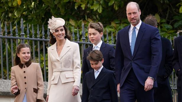 Prinz William und Prinzessin Catherine gehen mit ihren Kindern George, Charlotte und Louis vor einem Zaun spazieren.