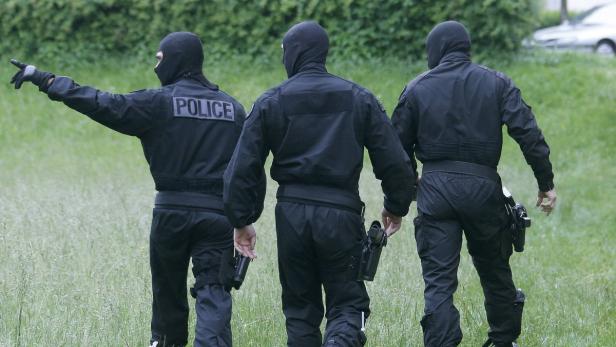 Drei Polizisten in schwarzer Uniform und Sturmhaube gehen über eine Wiese.