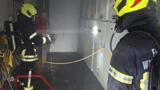Feuerwehrleute in Atemschutz kontrollieren einen verrauchten Schaltraum.
