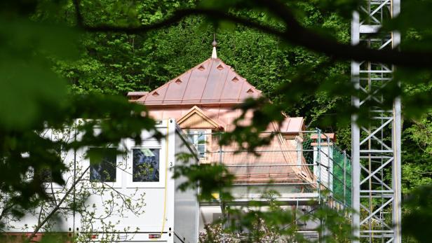 Baustelle mit Kupferdach zwischen dichtem Wald, im Vordergrund verdeckte Container und ein Metallgerüst.