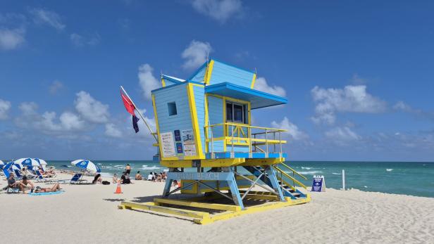 Bunte Rettungsschwimmerhütte am Strand von Miami Beach mit Sonne, Meer und Badenden.