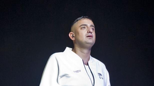 Rapper Haftbefehl mit Mikrofon in weißem Trainingsanzug auf dunkler Bühne.