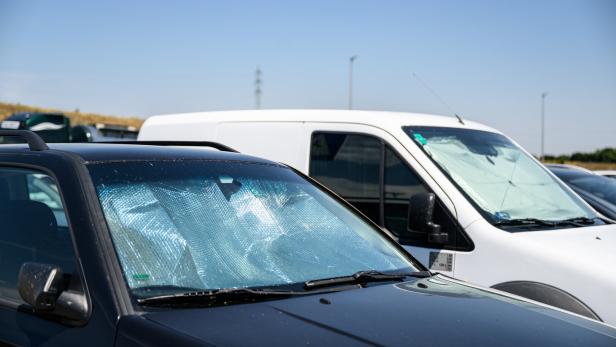 Mehrere geparkte Transporter und Autos mit Sonnenschutz an den Frontscheiben auf einem Parkplatz.