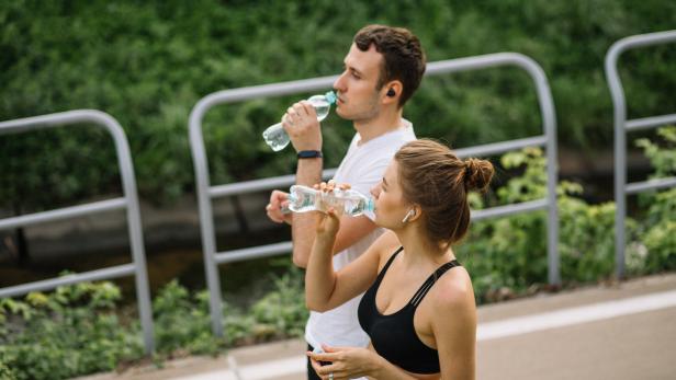 Zwei junge Menschen trinken während des Sports Wasser im Freien.