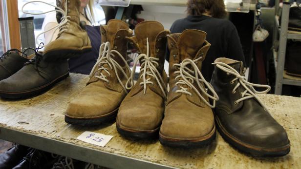 Mehrere Paare gebrauchte Stiefel und Schuhe stehen auf einem Regal zum Verkauf.