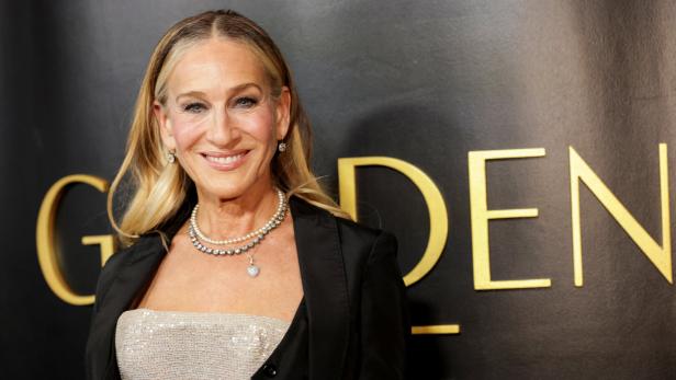 Sarah Jessica Parker lächelt vor einem schwarzen Hintergrund mit goldenem Schriftzug.