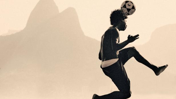 Ein junger Mann jongliert vor der Silhouette des Zuckerhuts in Rio de Janeiro einen Fußball mit dem Kopf.