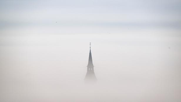 Kirchturmspitze ragt aus dichtem Nebel empor.
