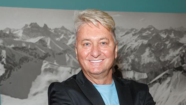Hubert Fella steht mit verschränkten Armen vor einer Bergfotografie.