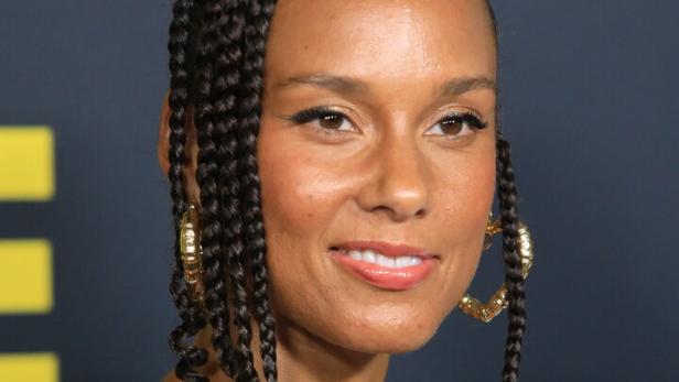 Alicia Keys lächelt in die Kamera, trägt ihre Haare zu einem hohen Dutt mit Zöpfen und große goldene Creolen.