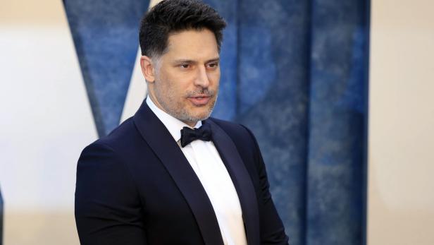 Joe Manganiello trägt einen dunklen Smoking mit Fliege vor einem blauen Hintergrund.