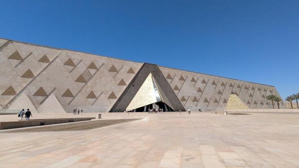 Die Fassade des Grand Egyptian Museum in Gizeh mit ihrem markanten dreieckigen Eingang vor einem klaren blauen Himmel.