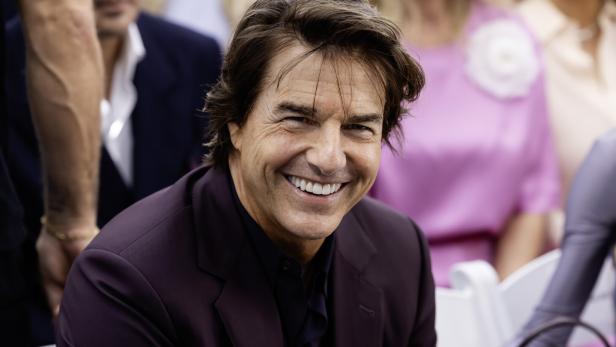 Tom Cruise lächelt in die Kamera, während er ein dunkles Sakko trägt.