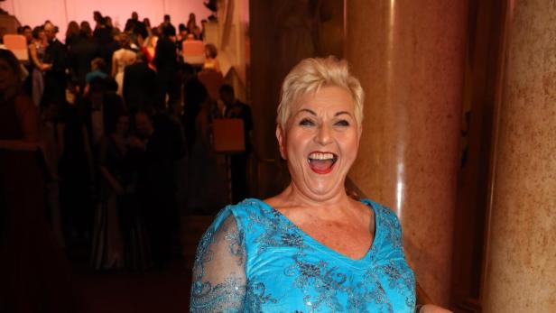 Eine lachende Frau in türkisfarbenem Abendkleid steht in einem festlich beleuchteten Saal.