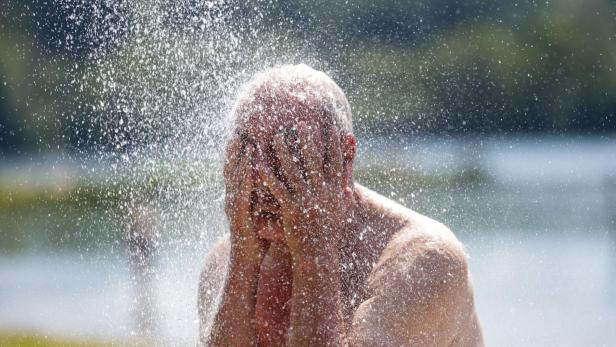 Ein Mann kühlt sich mit Wasserstrahlen ab und bedeckt im Hitzestress sein Gesicht.