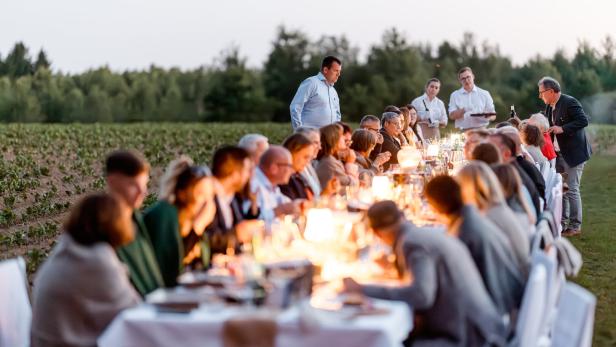 Lange Tafel mit Gästen und Kerzenlicht im Freien zwischen Feldern bei einer Abendveranstaltung der Waldviertler Tischkultur 2025.