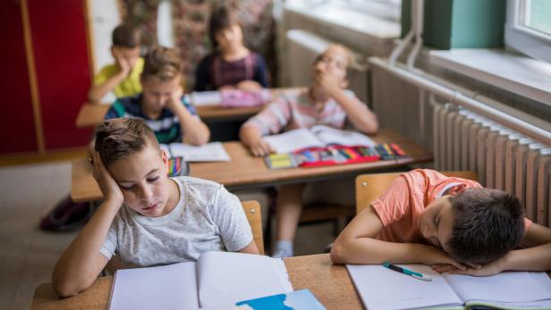 Erschöpfte Kinder sitzten in einem Klassenzimmer.