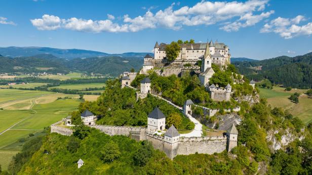 Die Burg Hochosterwitz thront auf einem bewaldeten Felskegel inmitten einer grünen Hügellandschaft in Kärnten.