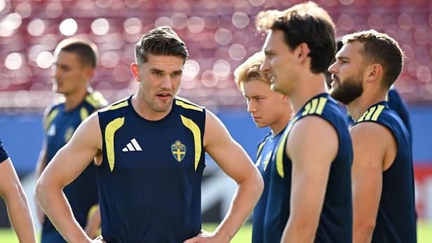 Spieler der schwedischen Fußballnationalmannschaft in dunkelblauen Trainingsshirts mit gelben Akzenten stehen auf einem Sportplatz.