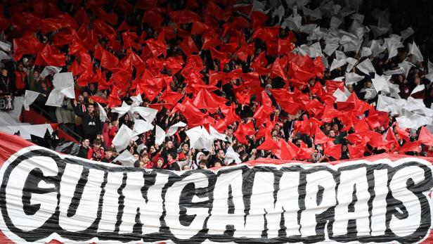 Fans von En Avant Guingamp schwenken im Stadion zahlreiche rote und weiße Fahnen hinter einem großen Banner mit der Aufschrift „GUINGAMPAIS“.