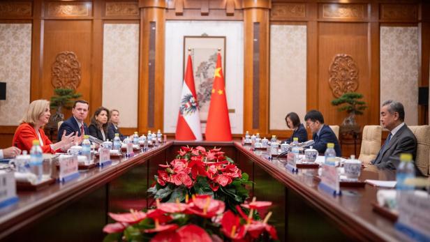 Delegationen verhandeln an einem langen Tisch in einem Holzsaal mit österreichischer und chinesischer Flagge.