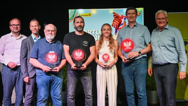 Sechs Personen stehen auf einer Bühne und halten Sporttrophäen vor einem Event-Hintergrund.