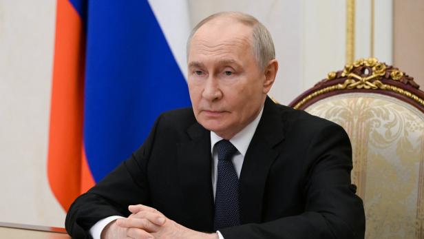 Wladimir Putin sitzt vor der russischen Flagge an einem Tisch mit Dokumenten.