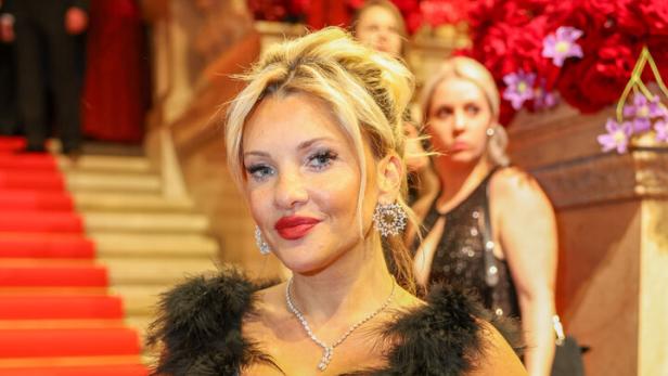 Evelyn Burdecki in einem schwarzen Federkleid steht vor einer mit roten Blumen geschmückten Treppe.