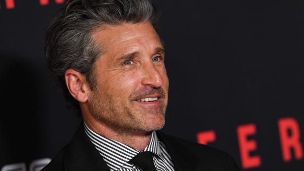Patrick Dempsey lächelt vor einem schwarzen Hintergrund mit roten Buchstaben.
