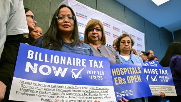 Mehrere Frauen bei einer Kundgebung halten Schilder für „Billionaire Tax Now“ und offene Krankenhäuser-Notaufnahmen.