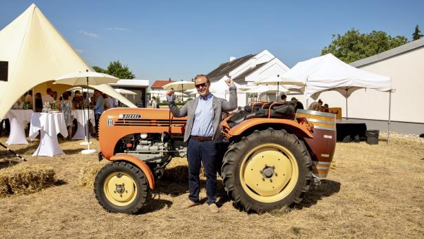 Mann posiert lächelnd neben einem orangefarbenen Diesel-Traktor auf einer Feier im Freien.