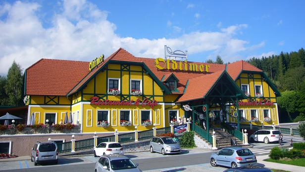 Das gelbe Oldtimer Restaurant & Café mit rotem Ziegeldach und Parkplatz davor unter blauem Himmel.