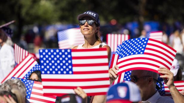 Eine Frau mit Sonnenbrille und einer „FREE“-Kappe hält bei einer Menschenmenge eine US-Flagge in die Höhe.