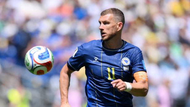 Edin Džeko spielt in einem blauen Trikot der bosnischen Nationalmannschaft mit der Nummer 11 und blickt konzentriert auf einen vorbeifliegenden Fußball.